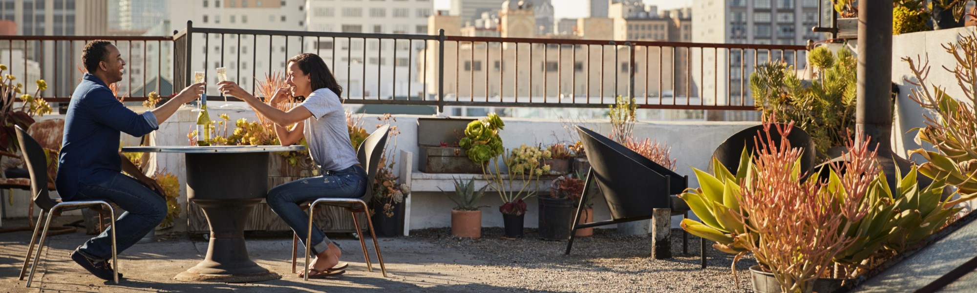 Couple drinking wine and making toast on rooftop with city skyline in background