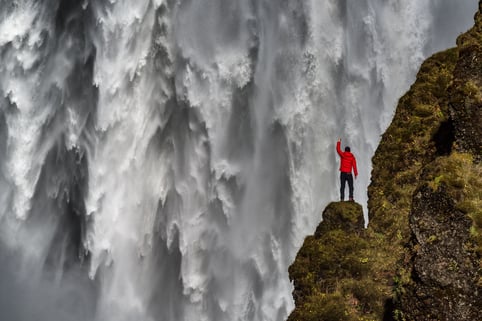 Man standing on rock next to a large waterfall.