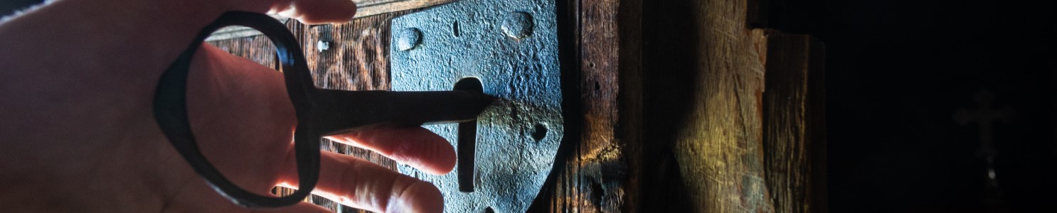 Hand turning ancient key in lock [1056497700] banner