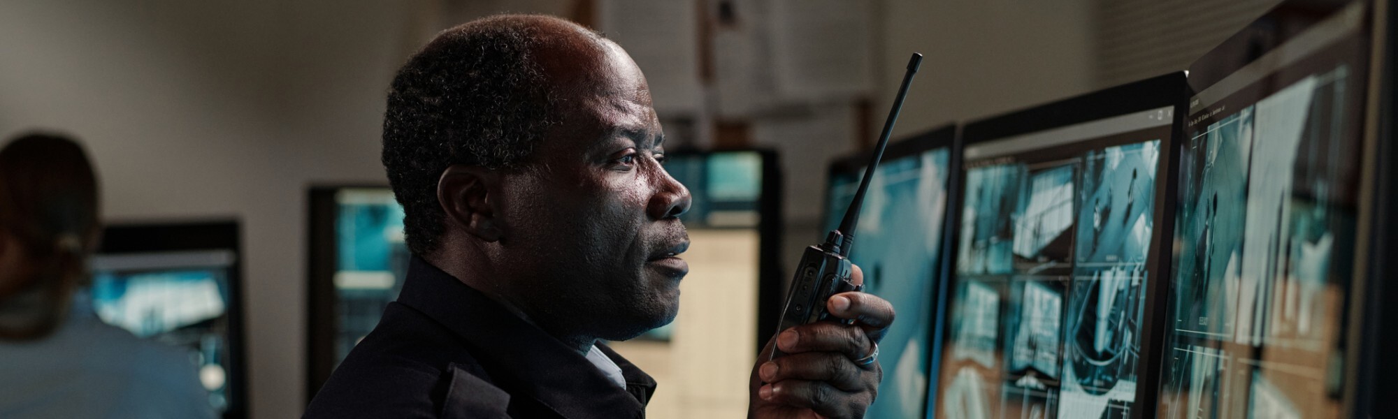 Mature man speaking on walkie-talkie while monitoring security cameras Mature man speaking on walkie-talkie while monitoring security cameras