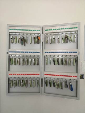 Image of open key cabinet hanging on beige wall. Several sets of keys are hanging on numbered key hooks