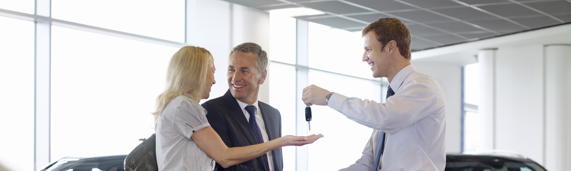 Salesman handing car keys to happy couple in showroom [108359372]