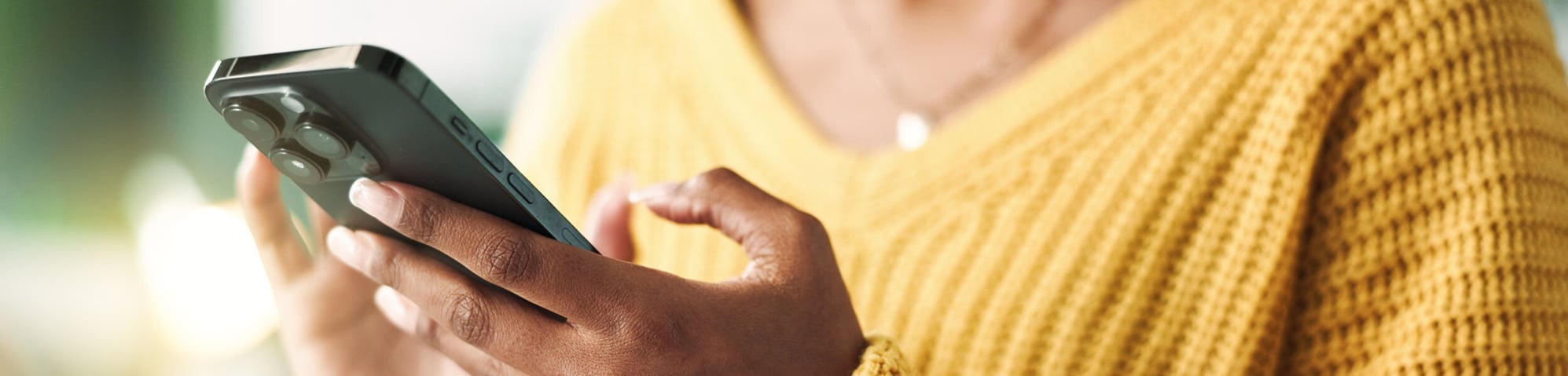 Woman in gold sweater typing on smartphone